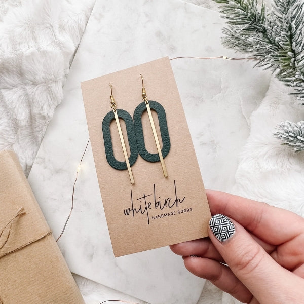 Pair of earrings on a 'White Birch Handmade Goods' card held by a hand with a patterned nail. | Green Leather Oval & Brass Bar Drop Earrings | whitebirch handmade | boogie + birdie