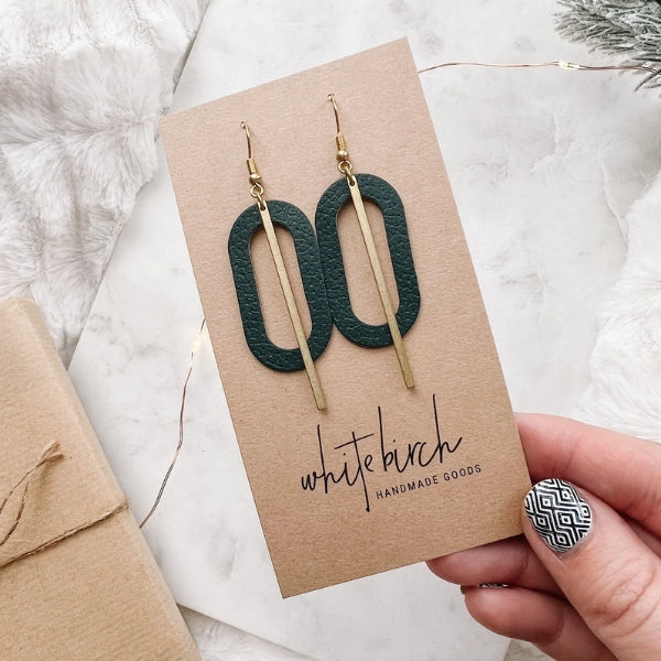 Pair of earrings on a 'White Birch Handmade Goods' card held by a hand with a patterned nail. | Green Leather Oval & Brass Bar Drop Earrings | whitebirch handmade | boogie + birdie