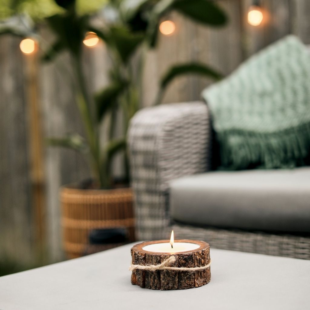 A lit candle is burning in the backyard with a Klippan blanket draped over a patio chair. Shop a selection of candles and cozy blankets at boogie + birdie in Ottawa